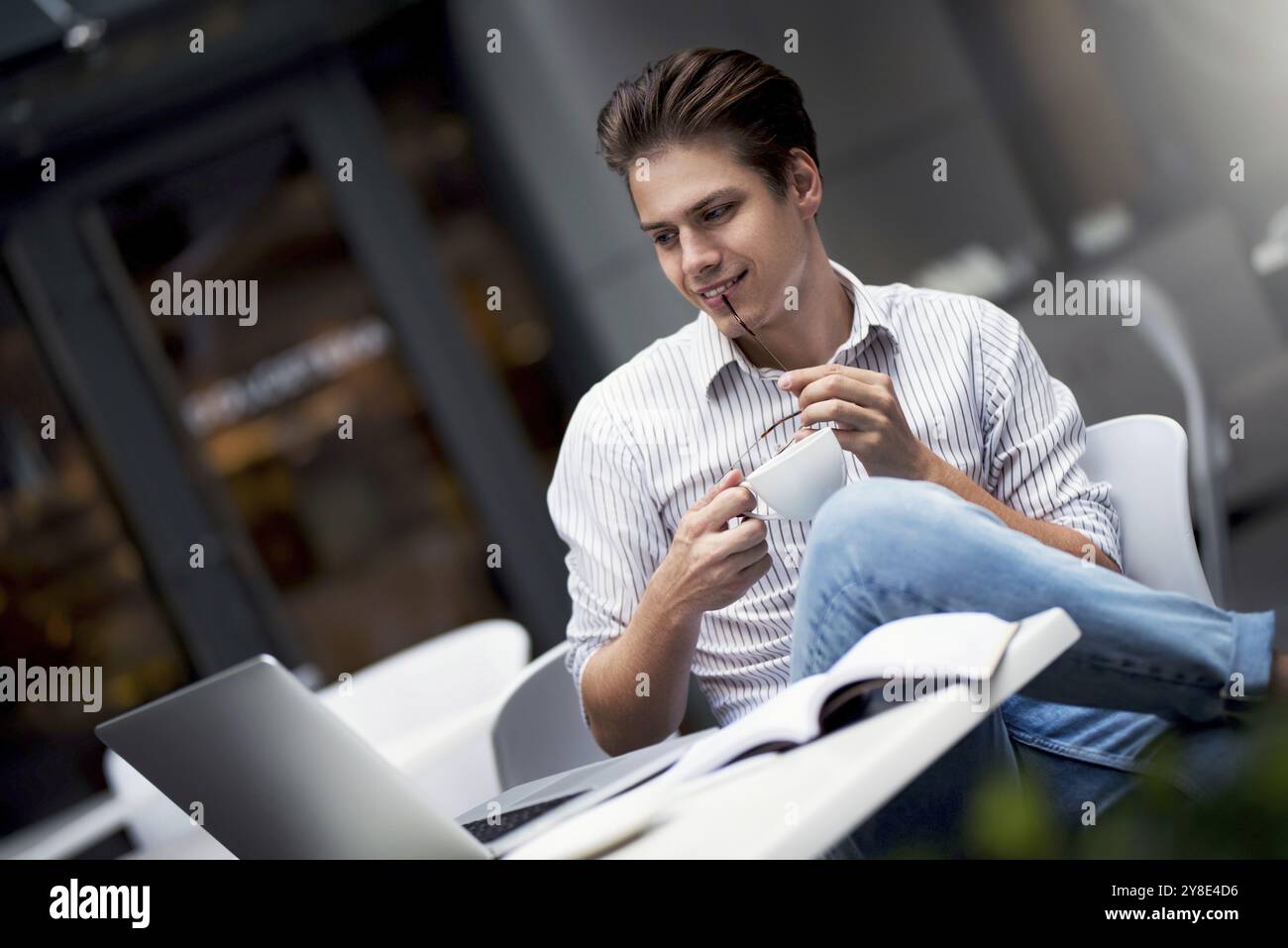 Hübscher junger Mann aus kaukasien, der am Laptop arbeitet und lächelt, während er Kaffee im Café genießt Stockfoto