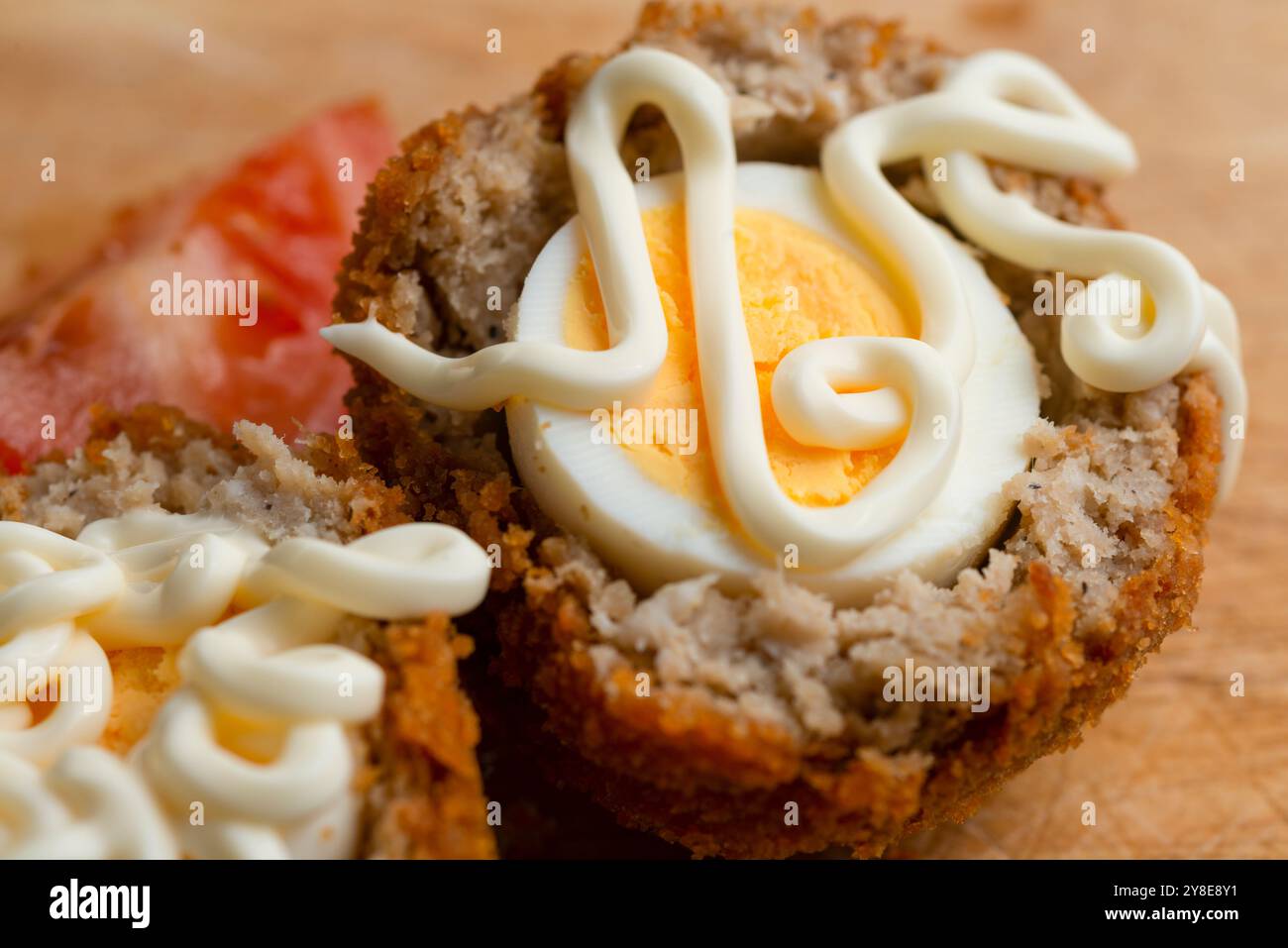 Frisch arrangierter, verzehrfertiger Mittagssnack mit Tomatenscheiben, auf einem hölzernen Schneidebrett mit Details von Gebäckbröseln und Texturen des Essens. Stockfoto