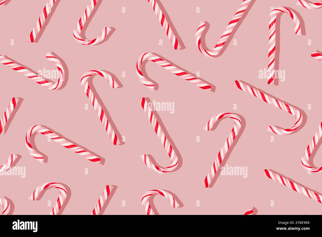 Ein nahtloses Muster aus rot-weiß gestreiften Bonbons, die zufällig auf einem rosa Hintergrund angeordnet sind. Stockfoto