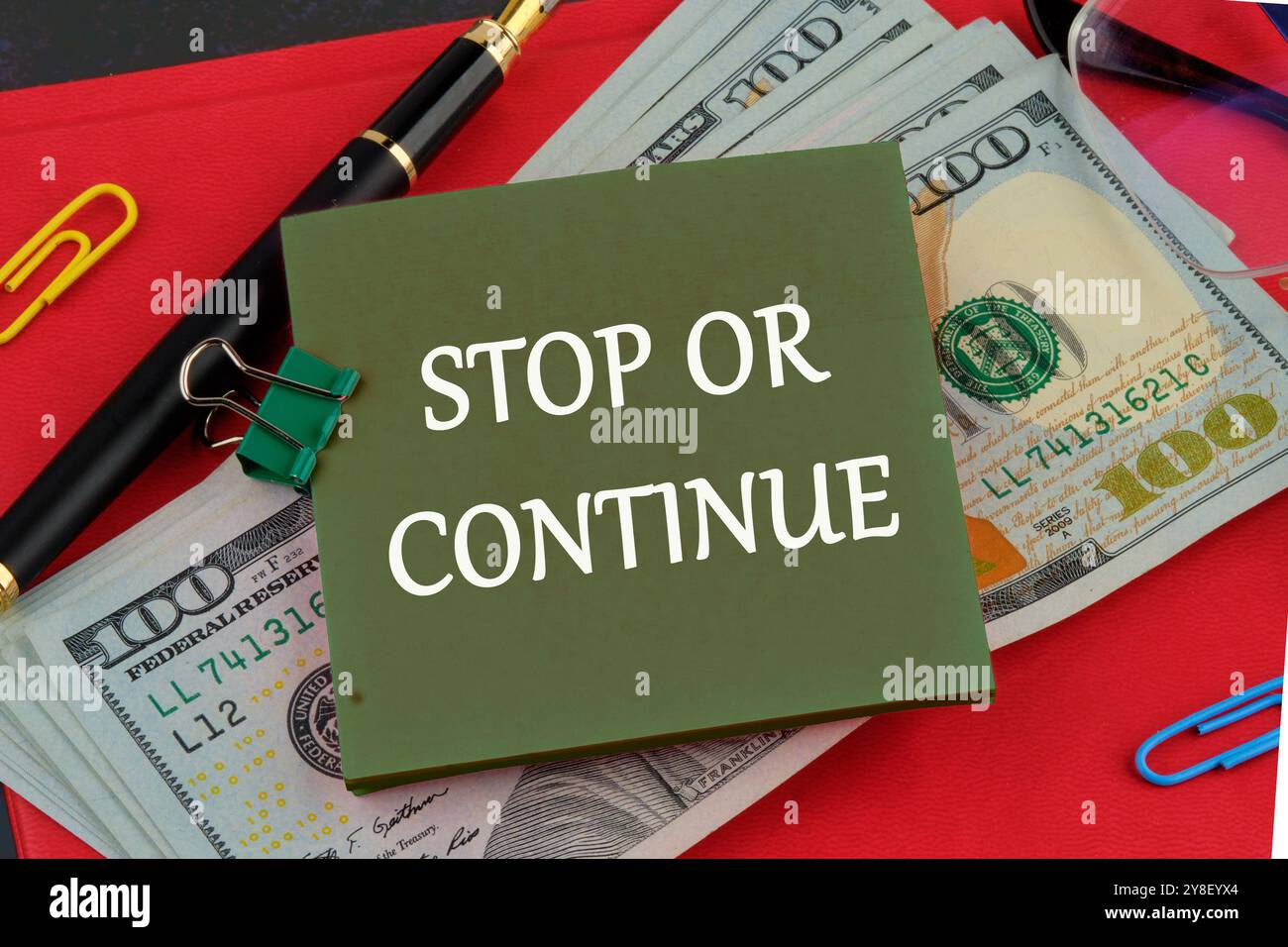 HALTEN SIE AN, ODER schreiben Sie auf einem grünen Aufkleber auf dem Hintergrund von Dollarscheine auf dem roten Buch. Stockfoto