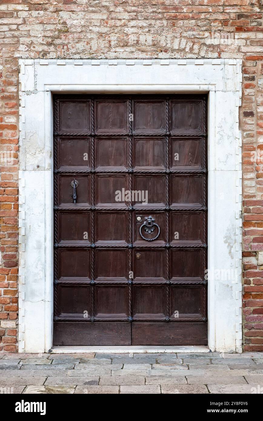 Tür in roter Backsteinmauer in Venedig. Italien. Antike Fassade. Alte Holztür in einem alten roten Backsteingebäude in Venedig, Italien. Stockfoto