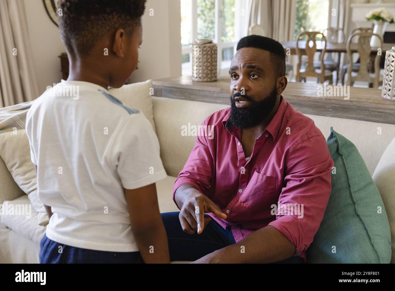 afroamerikanischer Vater sitzt auf dem Sofa im Wohnzimmer und diszipliniert seinen Sohn Stockfoto