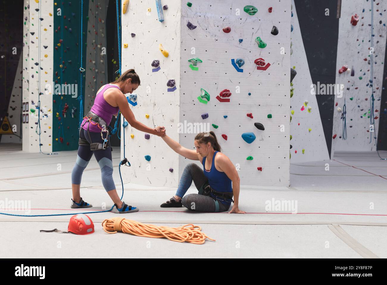 Zwei kaukasische Frauen an der Kletterwand, eine hilft beim Aufstehen Stockfoto