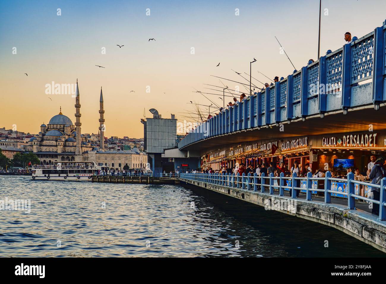 Turkiye. Istanbul. Sonnenuntergang über der Galata-Brücke in Istanbul, mit Fischern entlang der Geländer und der majestätischen Yeni-Moschee (neue Moschee) Stockfoto