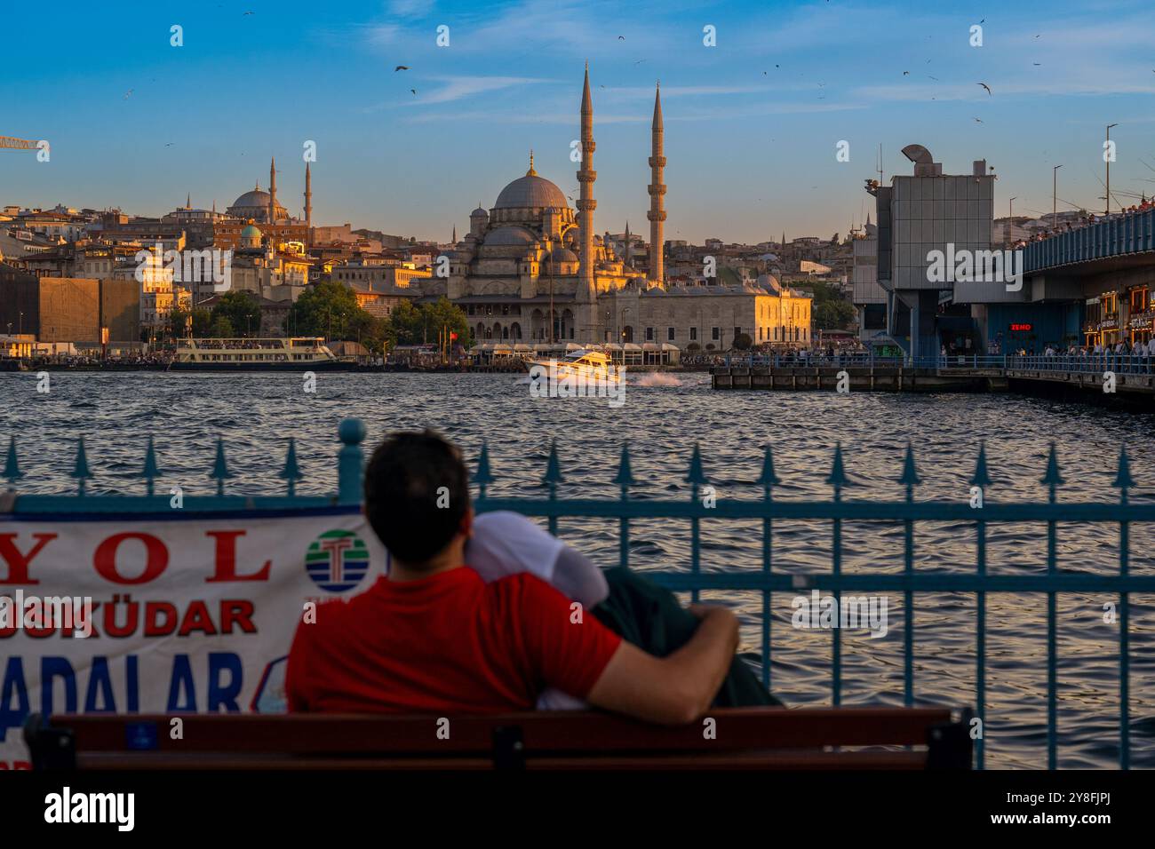 Turkiye. Istanbul. Ein Paar, das auf einer Bank sitzt, genießt den Sonnenuntergang über dem Bosporus mit Blick auf die herrliche Yeni Camii Moschee Stockfoto