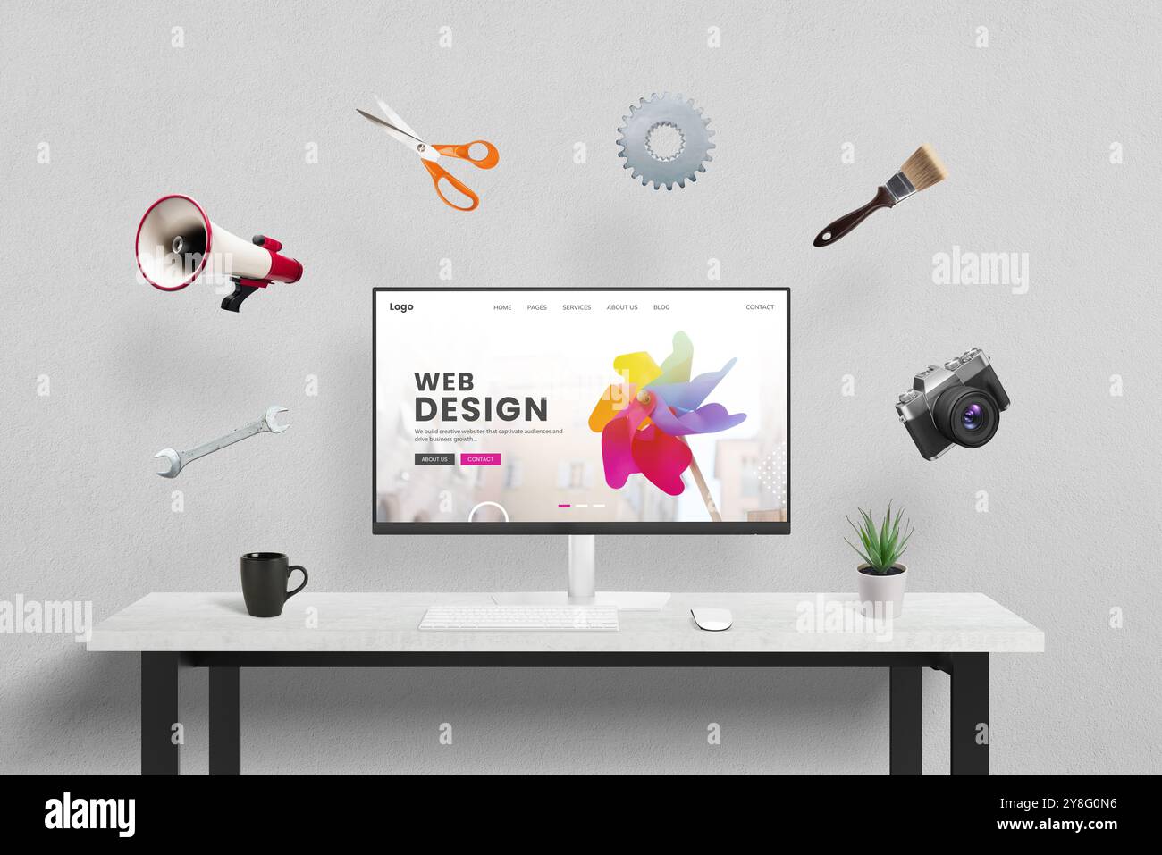 Webdesign-Konzeptseite, die auf dem Computer im Studio angezeigt wird, umgeben von kreativen, Marketing- und Bürowerkzeugen, die umherfliegen. Konzept des kreativen PR Stockfoto