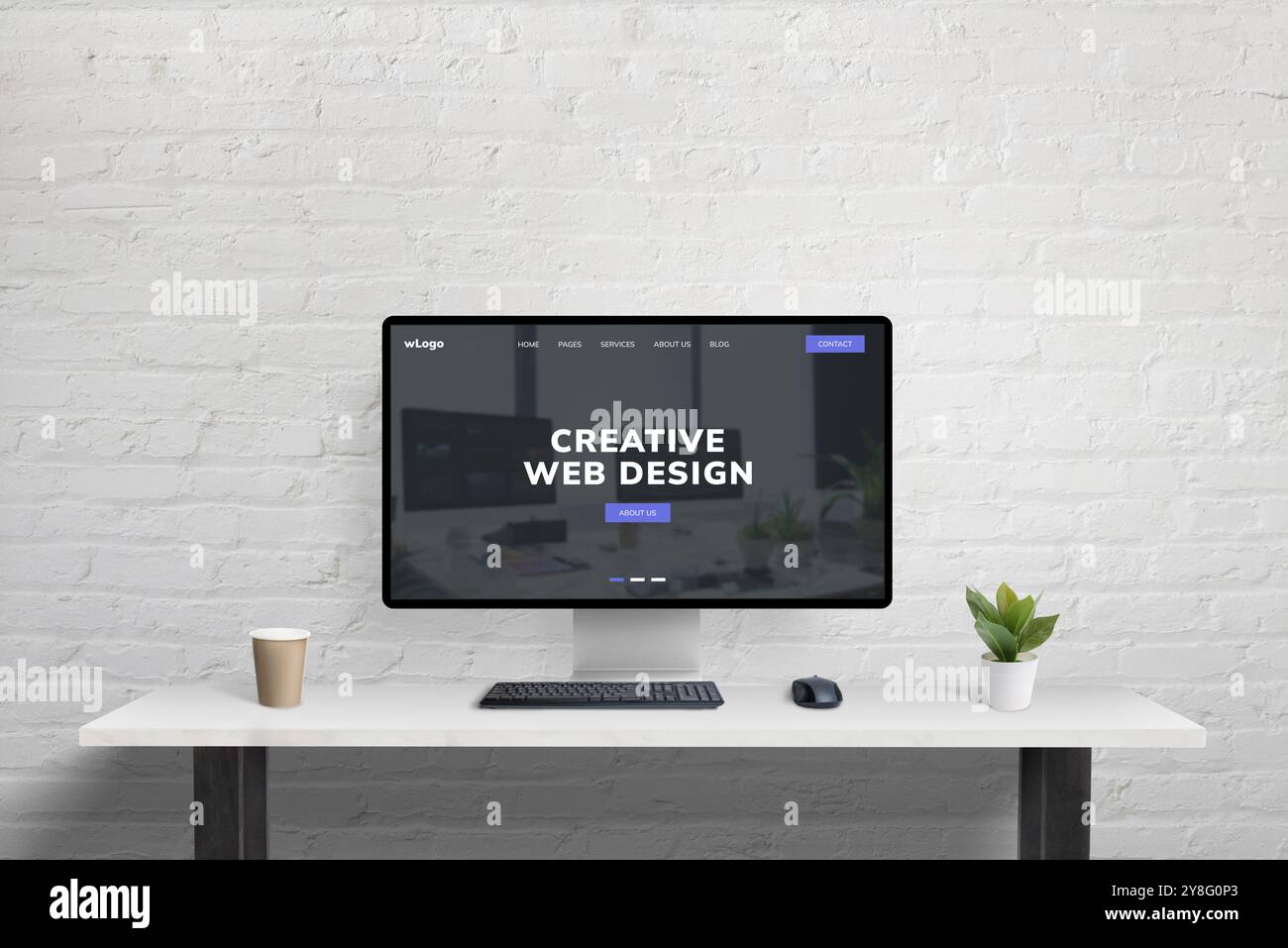 Saubere, kreative Web-Designseite aus Code Studio, die auf einem Computer an einem aufgeräumten Bürotisch mit Kaffee und Pflanze vor einem Background an einer Backsteinwand angezeigt wird Stockfoto