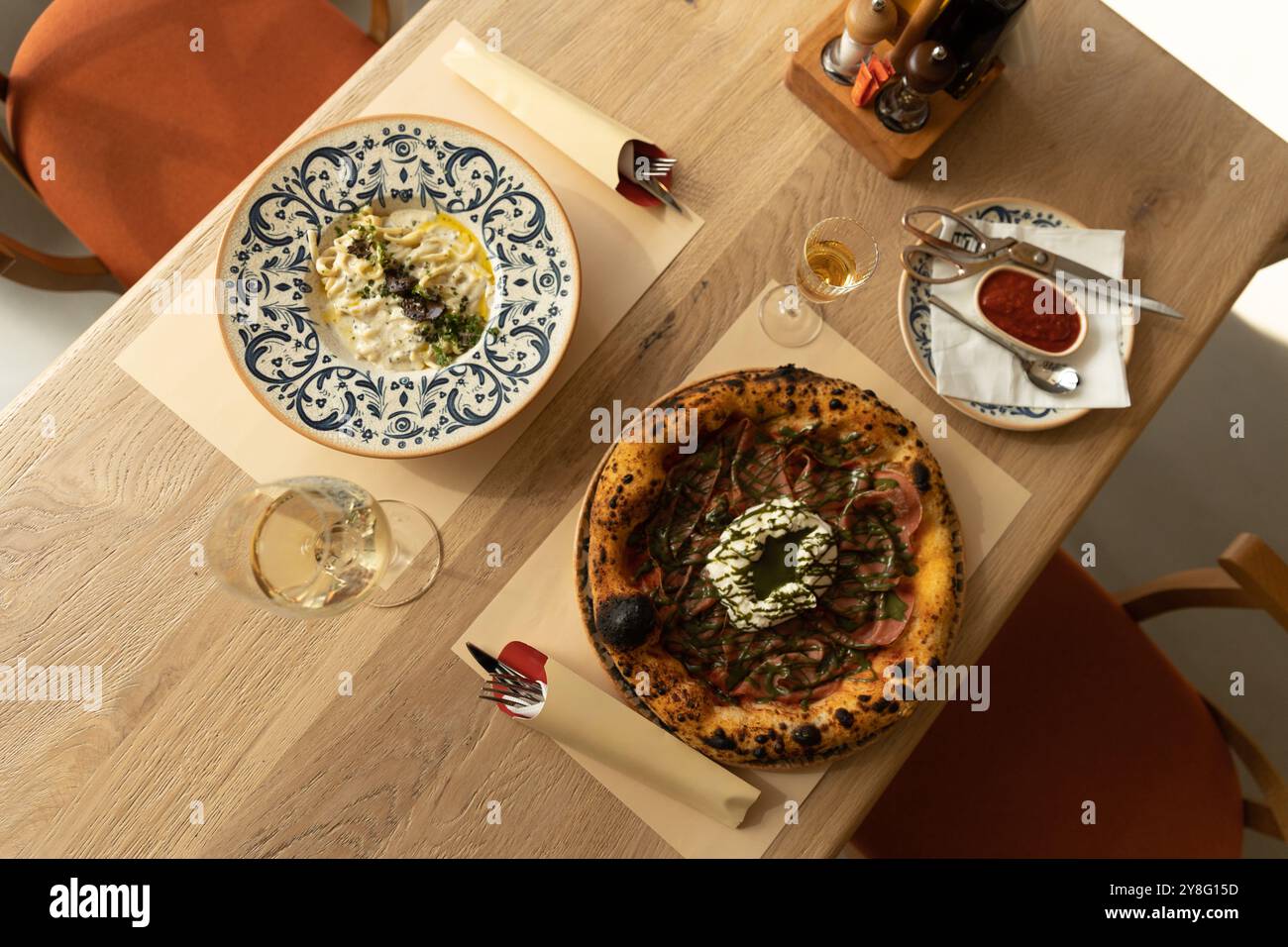 Genießen Sie eine köstliche Kombination aus Gourmet-Pizza mit frischen Zutaten und cremiger Pasta, perfekt präsentiert auf einem rustikalen Holztisch in A Stockfoto