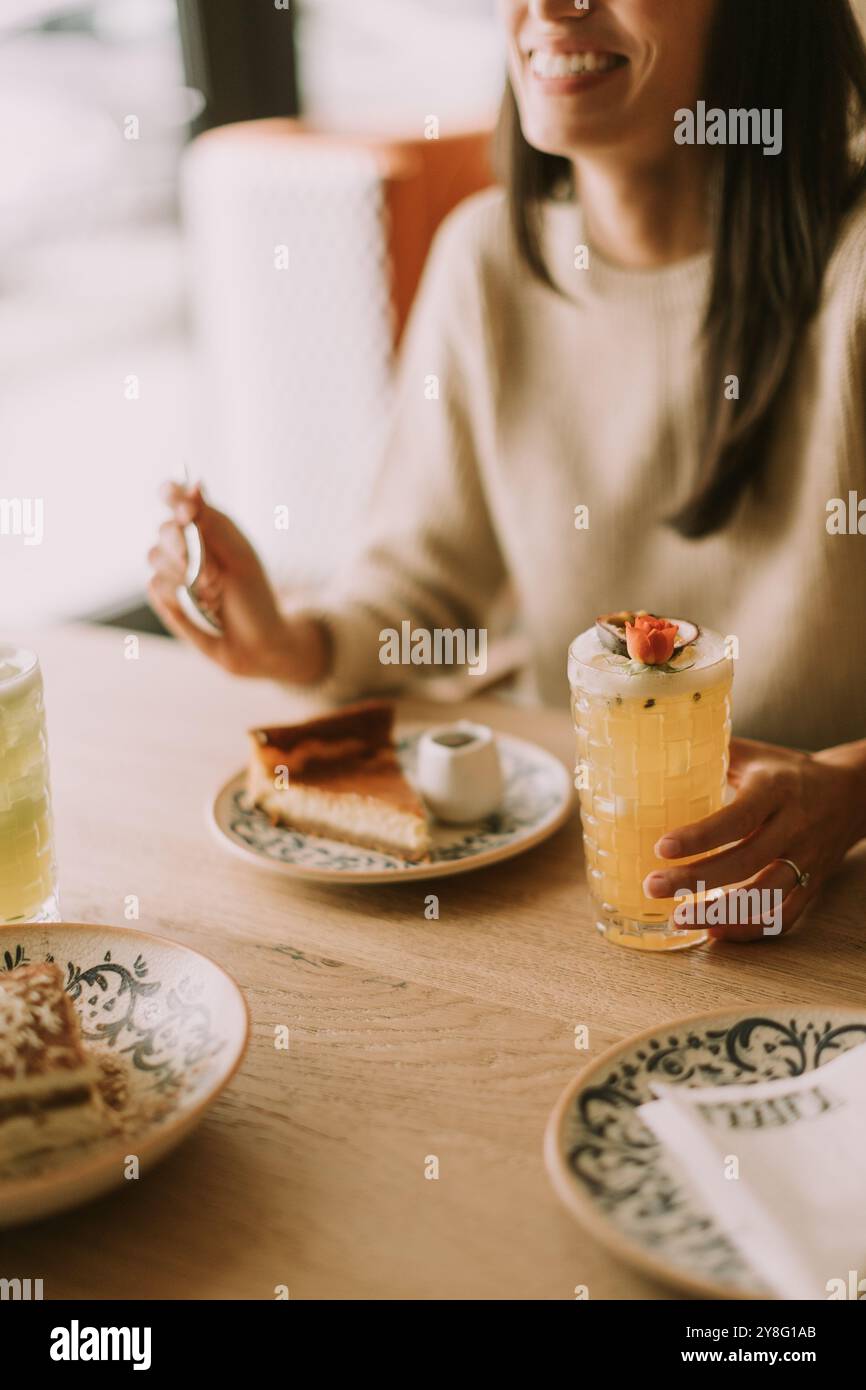 Eine Frau lächelt, während sie ein buntes Getränk hält, umgeben von köstlichem Essen. Freunde teilen Lachen und gemütliche Momente in einem charmanten Café während einer Leisu Stockfoto