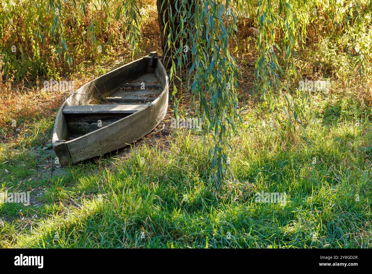 Ein altes Ruderboot, das an einem trockenen Uferufer verlassen wurde. Trockenes Flussbett an einem sonnigen Tag. Das Konzept des Klimawandels, der Dürre und des Austrocknens von Gewässern. Stockfoto