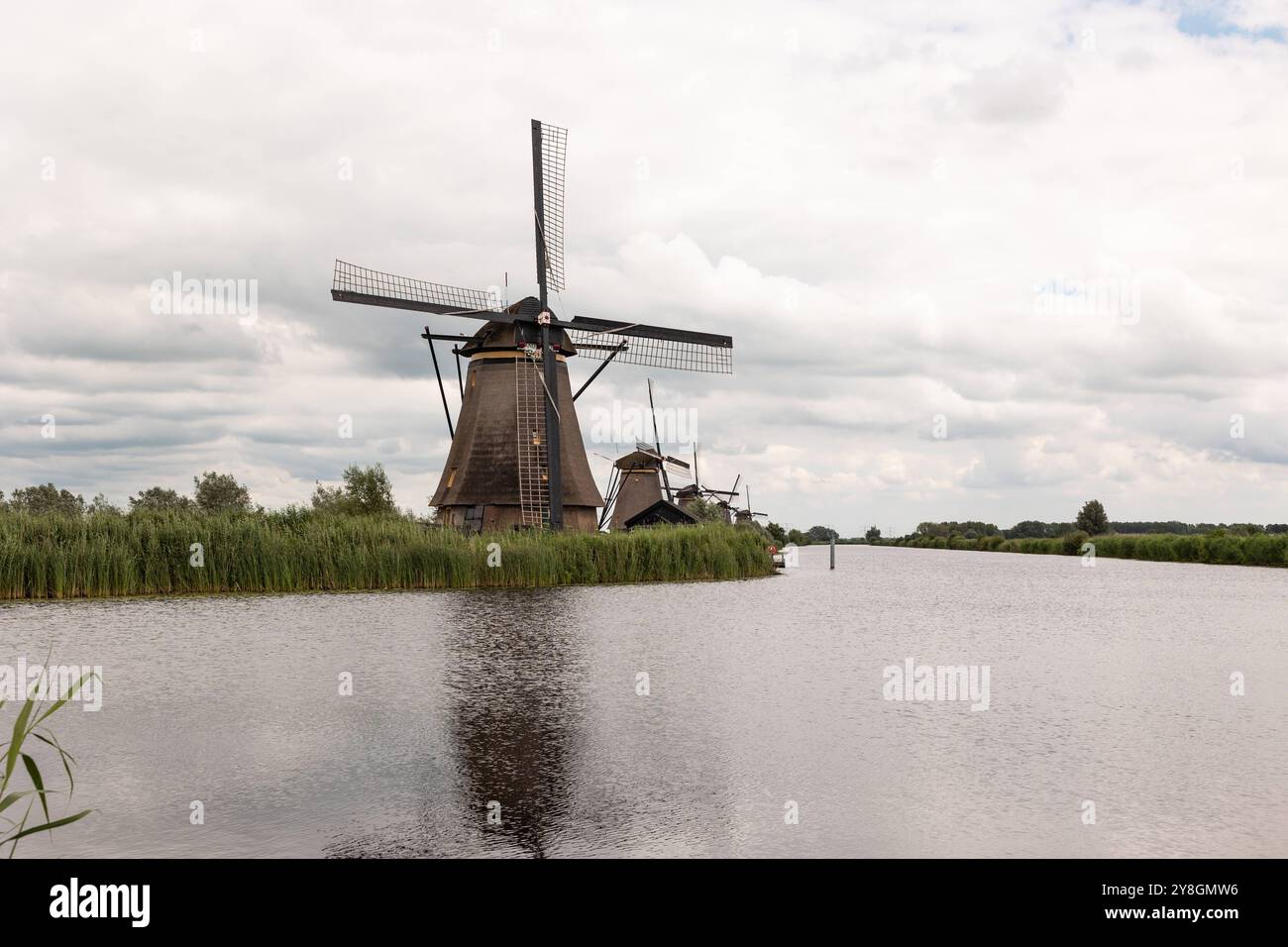 Gruppe historischer Windmühlen am Fluss, Reflexion im Wasser. Kinderdijk in den Niederlanden, bewölkter Tag. Reed Gras säumt das Ufer. niederlande kinderdijk B97A7672 Stockfoto