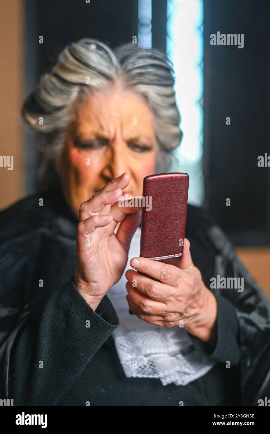 Die reife Richterin rundet die Stirn, während sie sich mit einem alten Klapptelefon Mühe macht, was die generationsbedingte Lücke in der Technologie unterstreicht Stockfoto