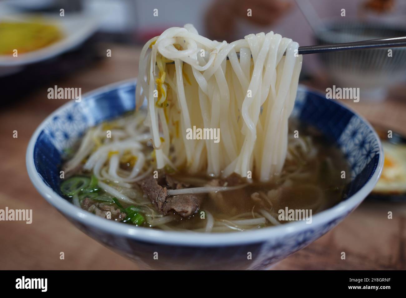 Vietnamesische Reisnudeln in einer Schüssel mit Stäbchen auf einem Holztisch Stockfoto