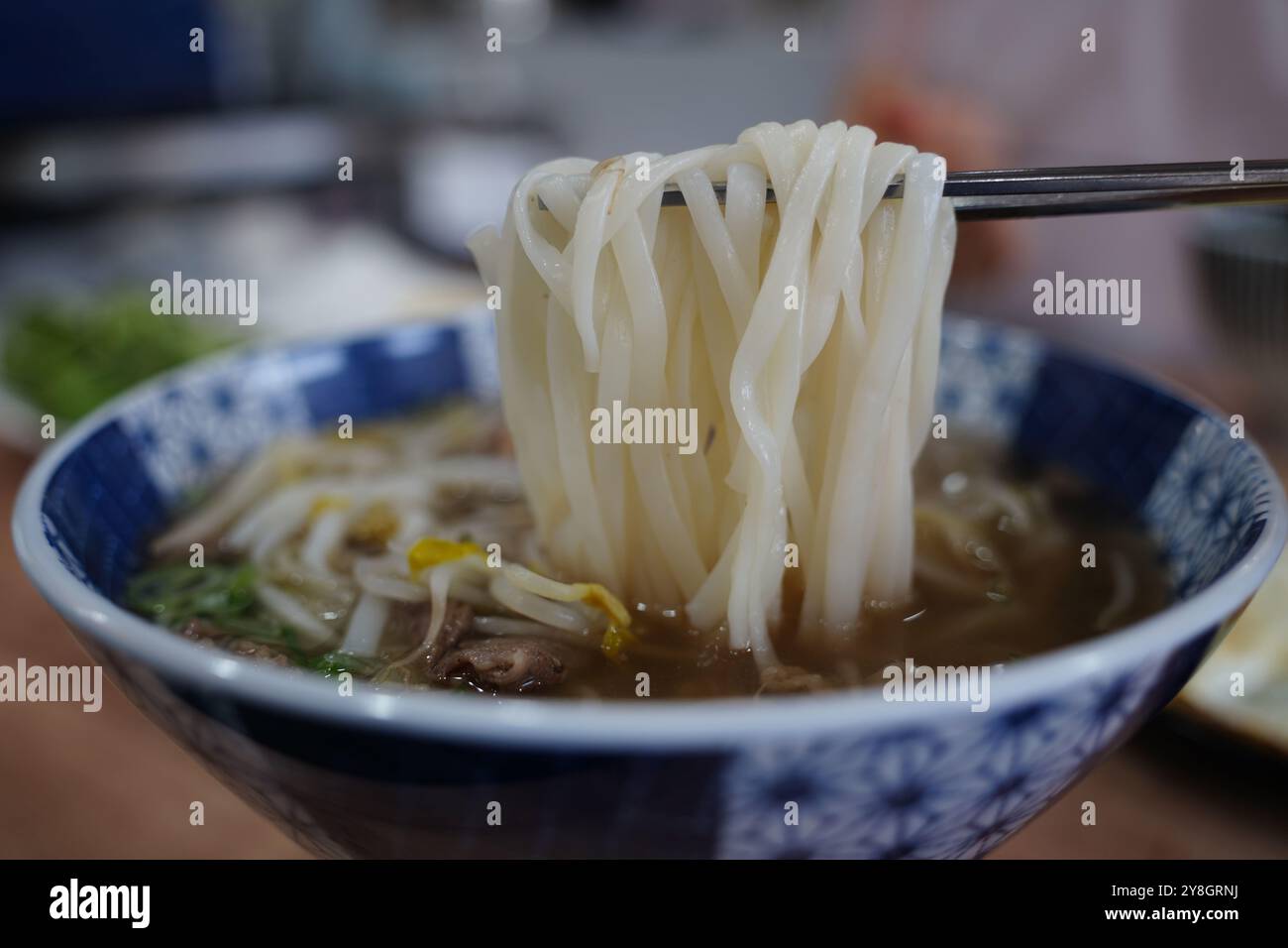 Vietnamesische Reisnudeln in einer Schüssel mit Stäbchen auf einem Holztisch Stockfoto