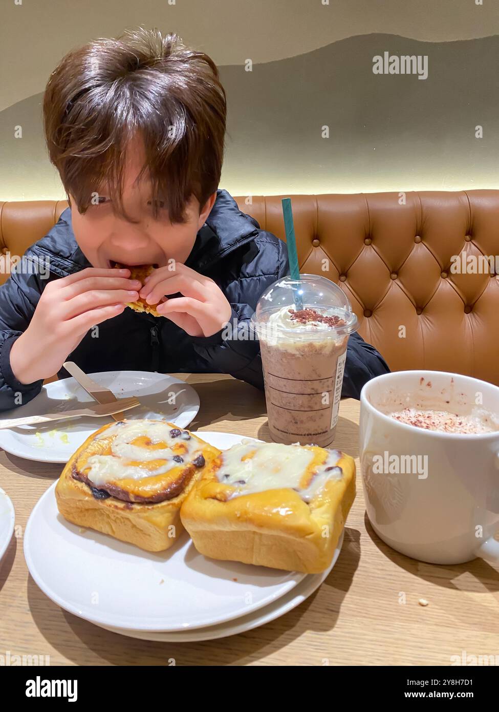 Junge beim Mittagessen in einem Starbucks Café mit Zimtrollen zum Nachtisch - Smartphone-aufgenommenes Stockfoto