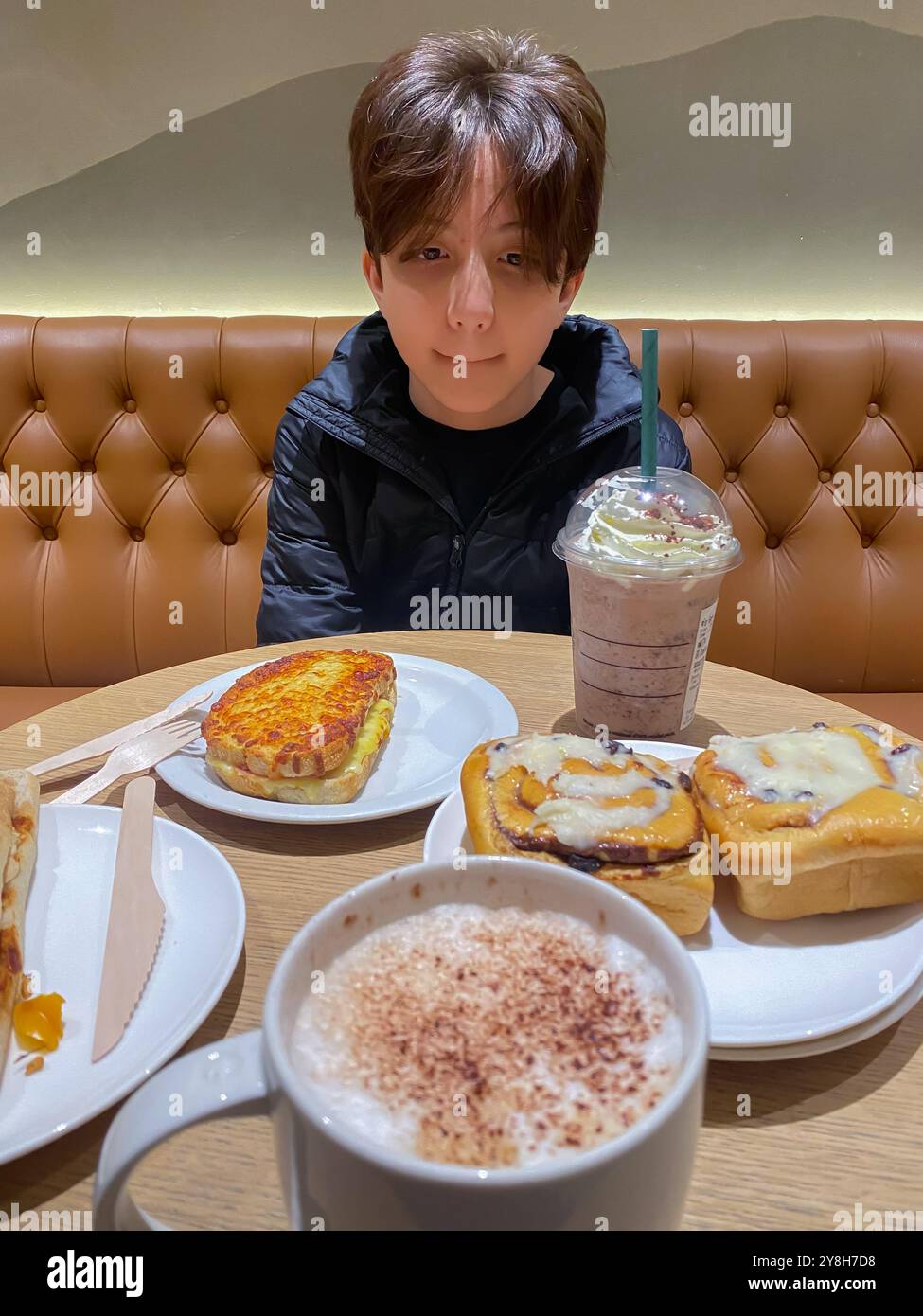 Junge beim Mittagessen in einem Starbucks Café mit Zimtrollen zum Nachtisch - Smartphone-aufgenommenes Stockfoto