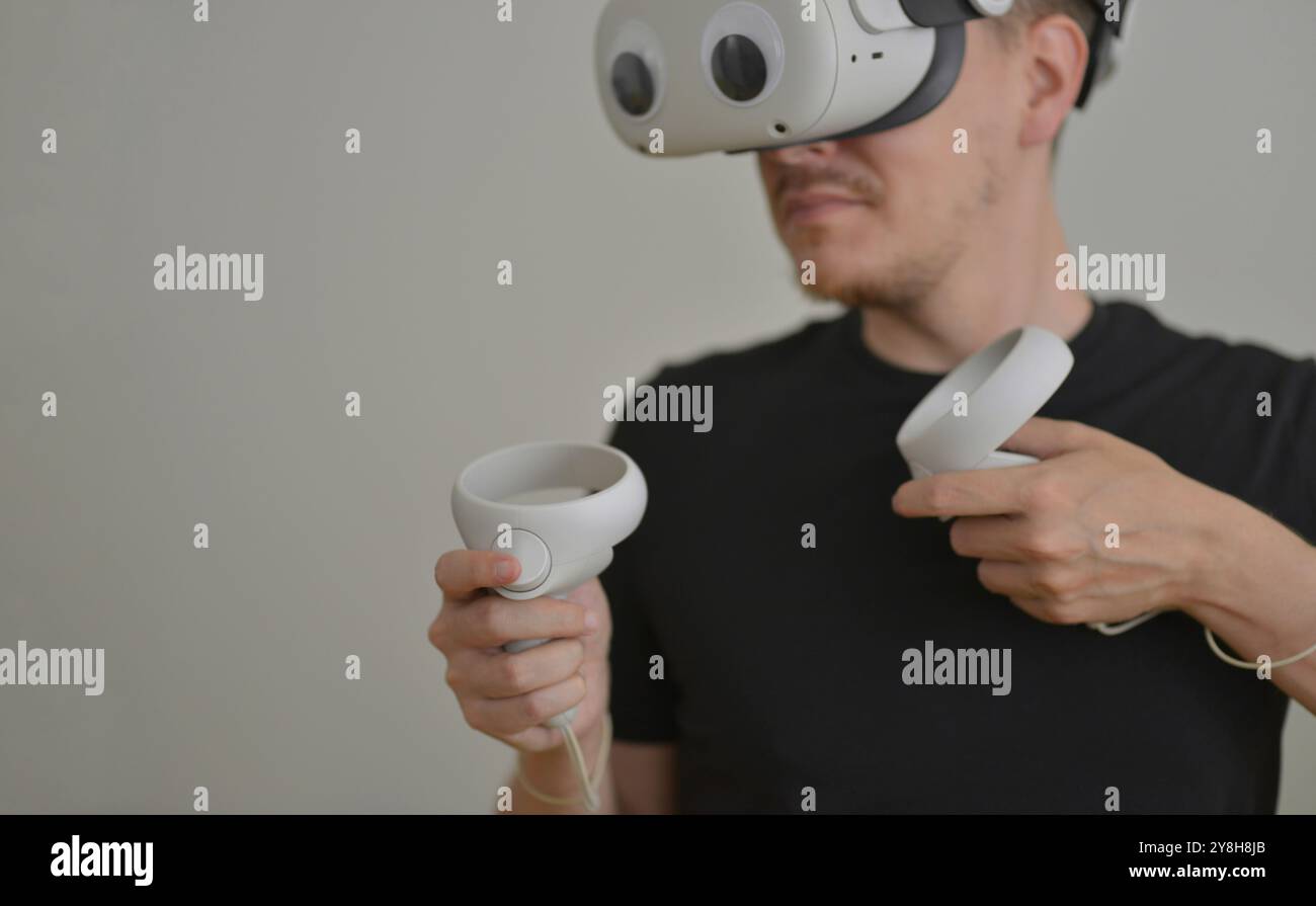 Ein junger Mann, der visuelle Reality-Brillen mit Augenaufklebern spielt. VR-Headset-Brille, die Metaverse mit Joysticks verbindet. Futuristische Cyberspace-Technologie Stockfoto