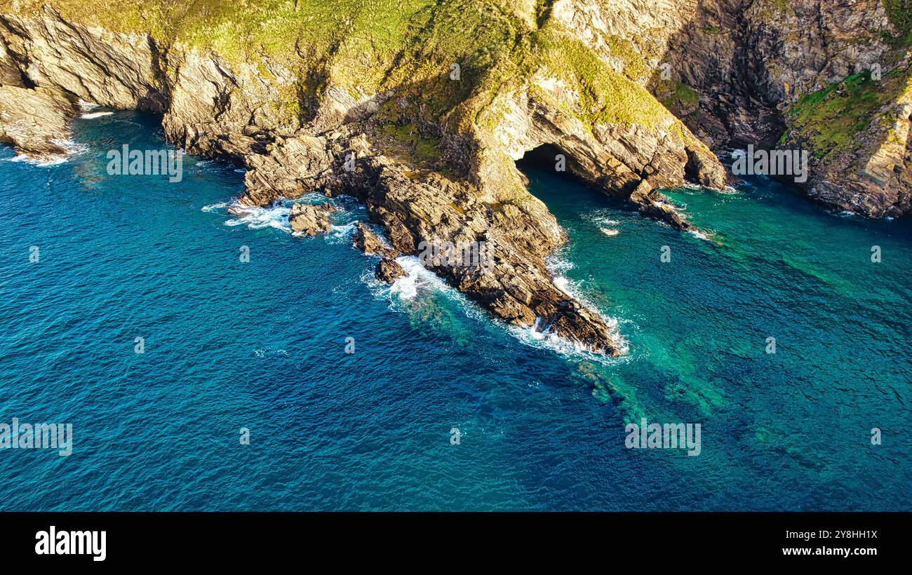 Blick aus der Vogelperspektive auf die felsige Küste mit klarem türkisfarbenem Wasser. Die Landschaft verfügt über zerklüftete Klippen und einen natürlichen Bogen, der durch Erosion geformt wurde. Kurven sanft cr Stockfoto