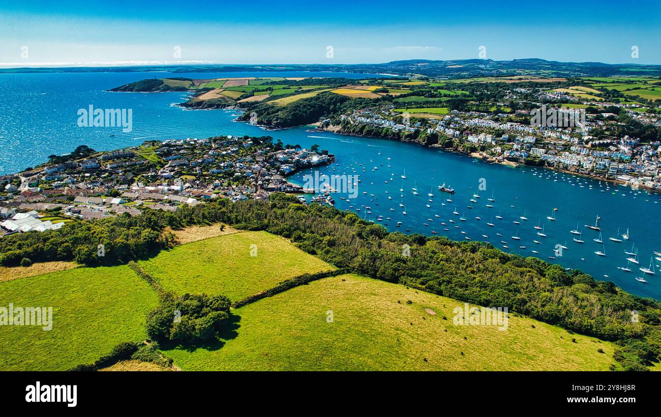 Aus der Vogelperspektive auf eine Küstenstadt, umgeben von üppigen grünen Feldern und einer ruhigen blauen Bucht mit Booten. Die Landschaft bietet sanfte Hügel und eine Clea Stockfoto