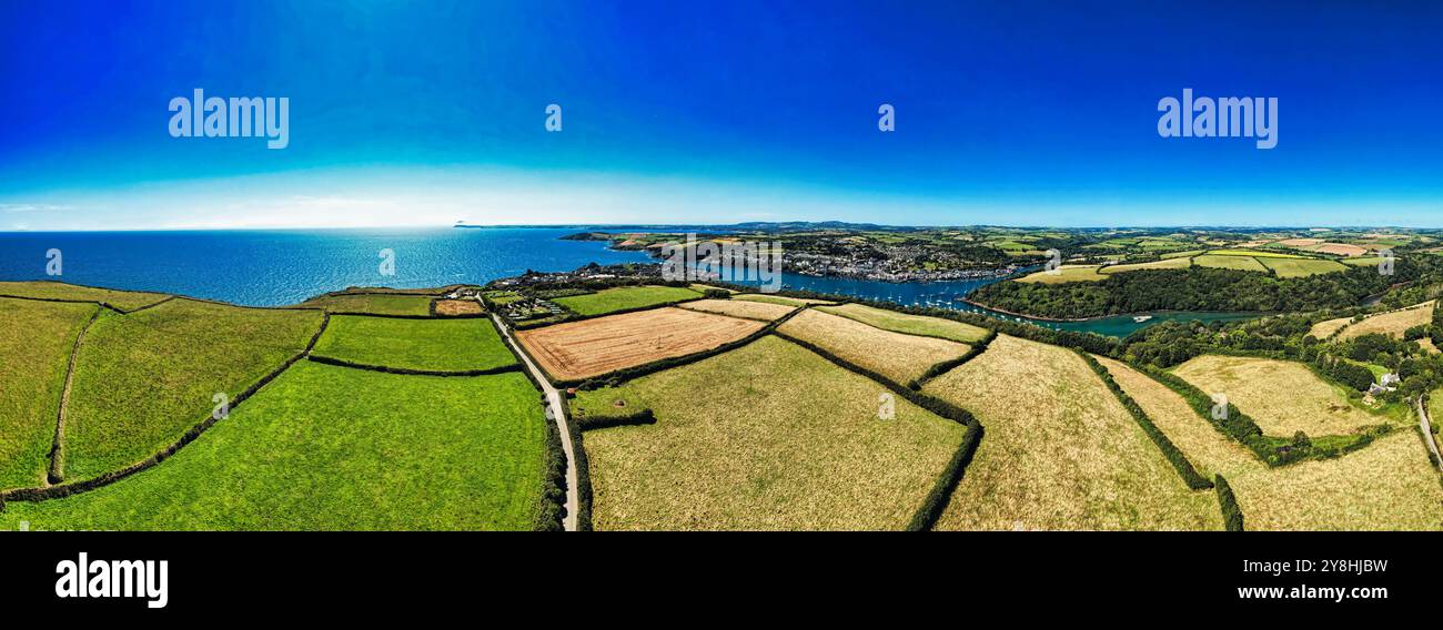 Ein Panoramablick auf eine Küstenlandschaft mit üppigen grünen Feldern, einem Fluss und einer entfernten Stadt am Meer unter einem klaren blauen Himmel. Stockfoto