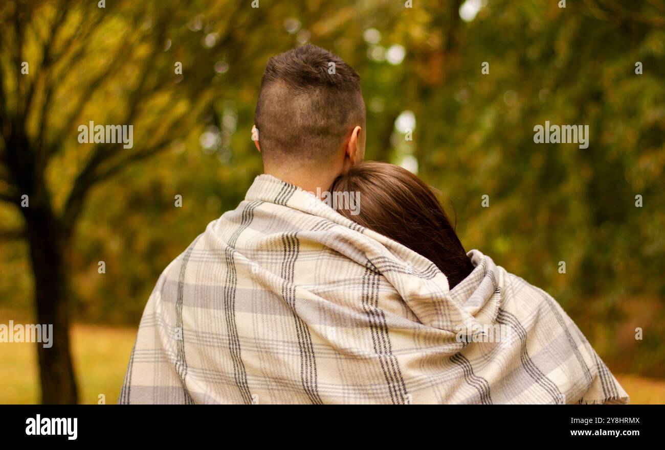 Ein junges verheiratetes Paar steht mit dem Rücken zur Kamera, bedeckt mit einer Decke vor dem Hintergrund des Herbstlaub Stockfoto