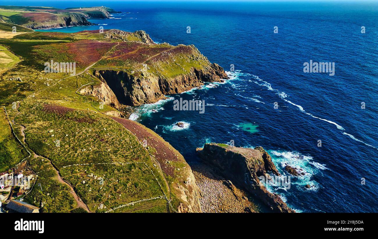 Aus der Vogelperspektive auf eine zerklüftete Küste mit Klippen und lebhaften grünen Hügeln. Das Meer ist tiefblau, mit Wellen, die gegen das felsige Ufer stürzen. Der Landsc Stockfoto