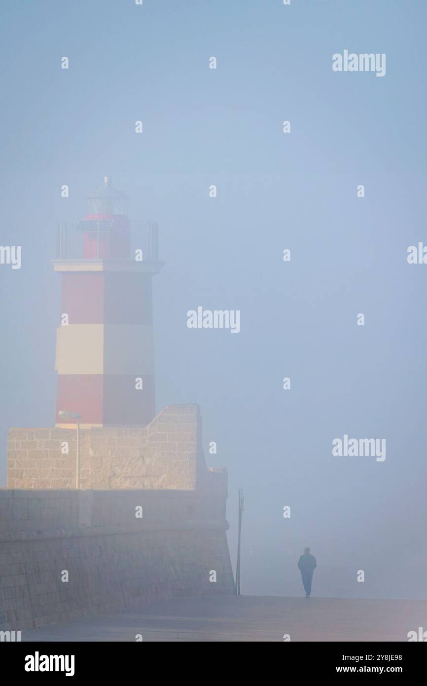 Silhouette eines Mannes, der an einem nebeligen Morgen entlang der Promenade in der Nähe des historischen Leuchtturms von Monopoli, Italien, spaziert. Stockfoto