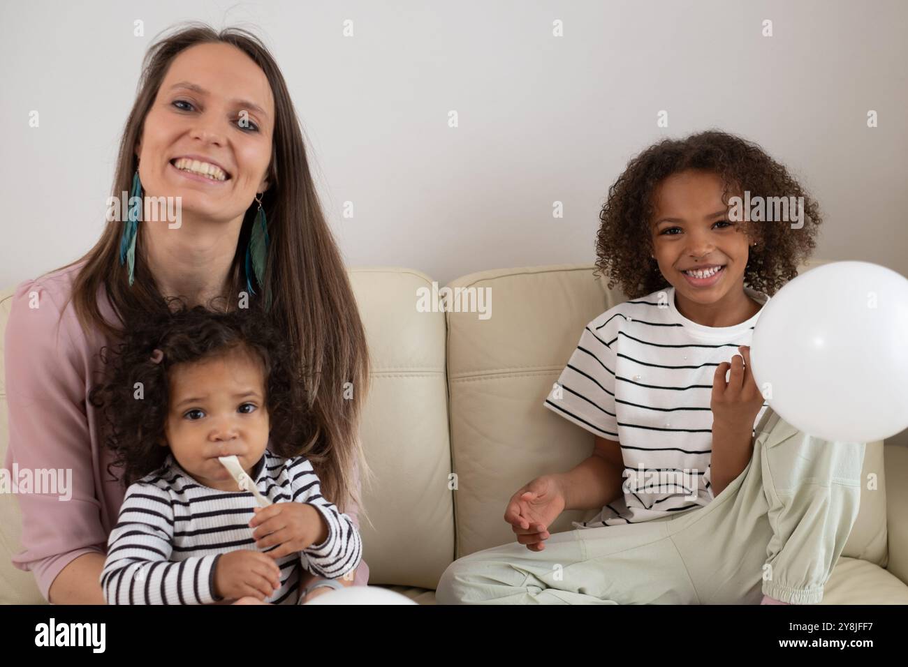 Lächelnde Mutter mit Kindern auf dem Sofa, verspielte Momente, Familienbande zeigen, glücklich im Wohnzimmer, fröhlichen Ausdruck zeigen, Mutterschaft Co Stockfoto