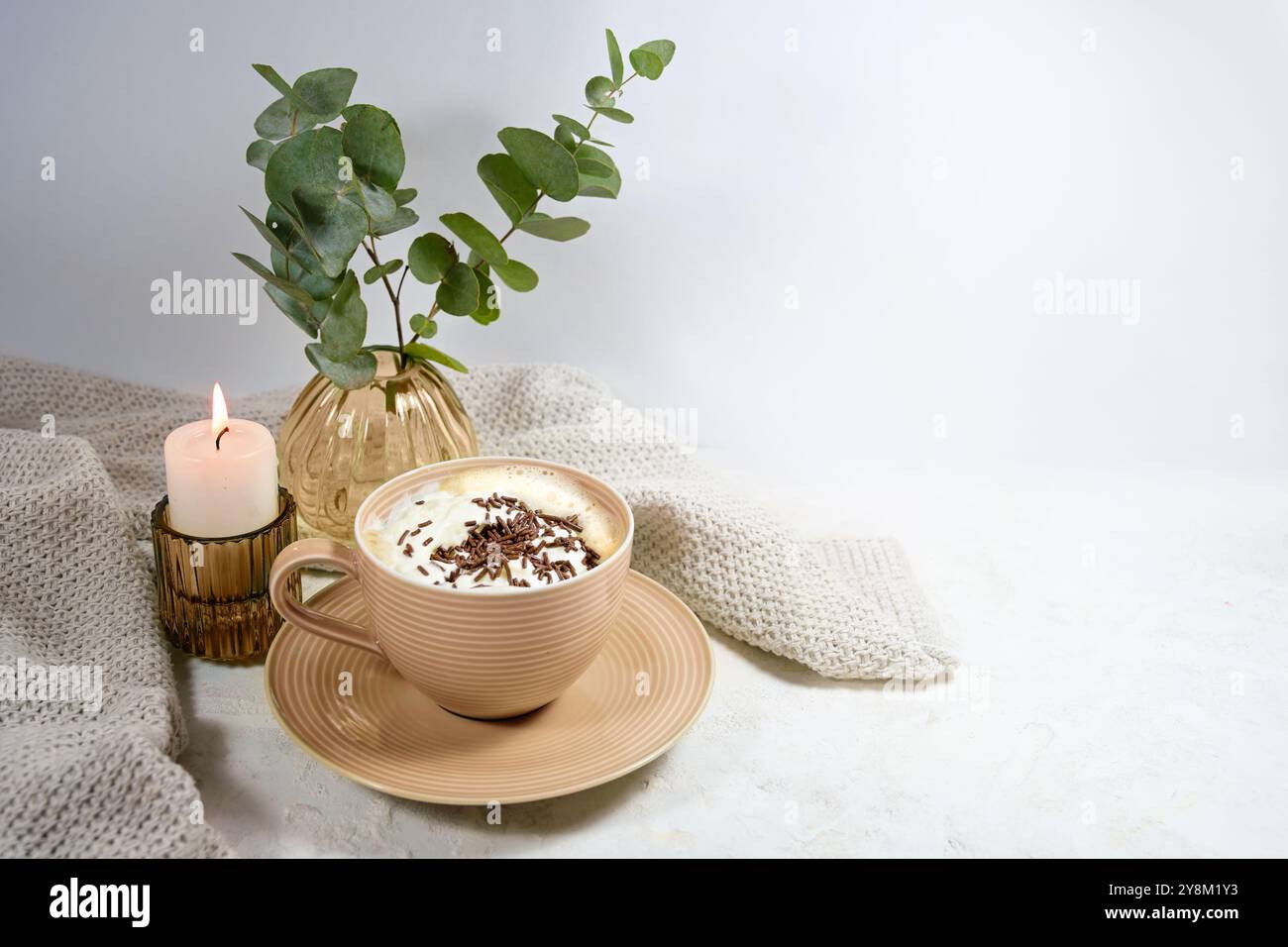 Tasse heiße Schokolade oder Cappuccino mit Schlagsahne, Kerze und einer Vase mit Zweigen, süßes Getränk für kalte Tage in einem gemütlichen Zuhause, heller Hintergrund, Kopie Stockfoto