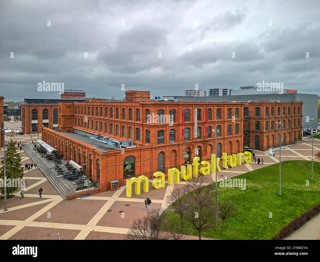 Renoviertes Industriegebäude aus rotem Backstein in Manufaktura, Łódź, Polen, mit auffälliger gelber Beschilderung und Stadtplatz an einem bewölkten Frühlingstag Stockfoto