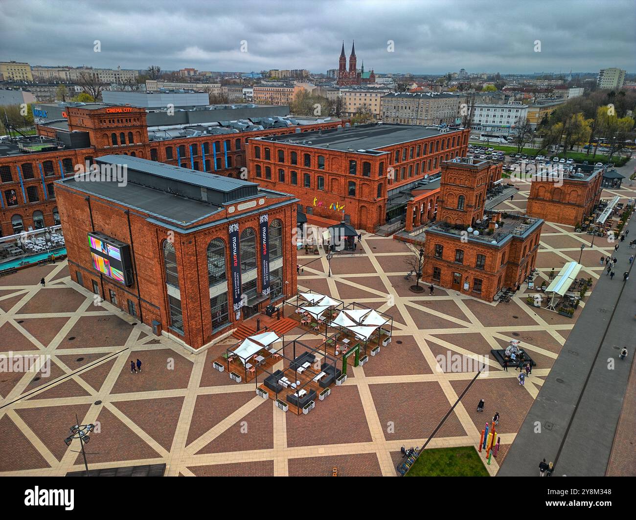 Renoviertes Industriegebäude aus rotem Backstein in Manufaktura, Łódź, Polen, mit auffälliger gelber Beschilderung und Stadtplatz an einem bewölkten Frühlingstag Stockfoto