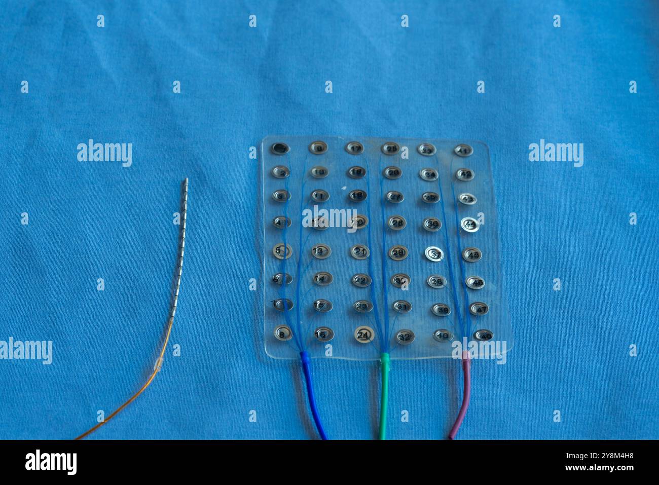 Nahaufnahme eines subduralen Gittergitters und einer einzelnen Stereoelektroenzephalographie- oder SEEG-Elektrodenableitung auf blauer steriler Oberfläche. Stockfoto