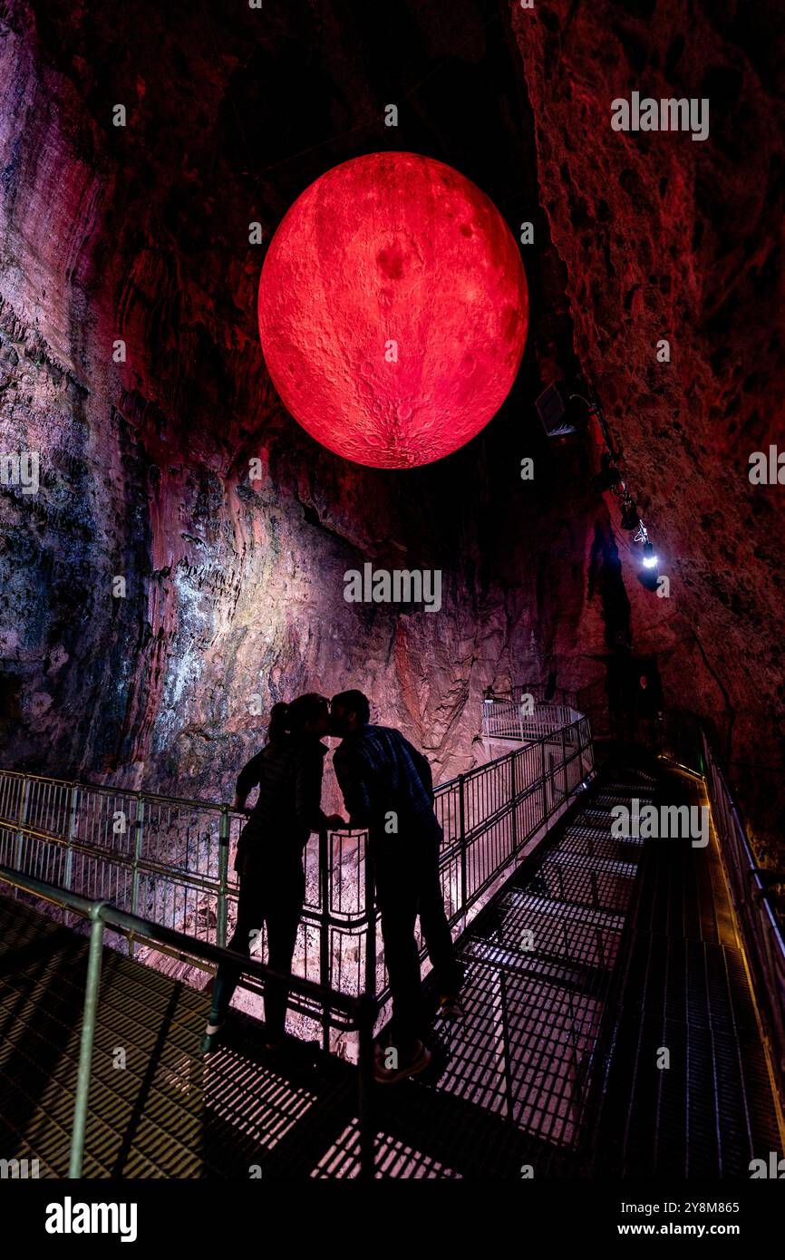 Ein paar Küsse in Kammer 9 in den Höhlen von Wookey Hole, in der Nähe von Wells in Somerset, wo ein riesiger 5 m breiter Blutmond vom Dach der Höhle hängt, als Teil der jährlichen Feier von Wookey Hole zu Halloween-Veranstaltungen. Bilddatum: Sonntag, 6. Oktober 2024. Stockfoto