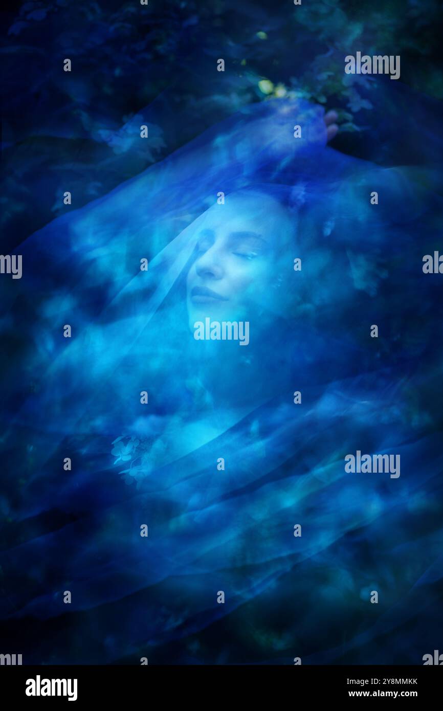 Eine tanzende Frau zeigt im Sommer bei Hortensia Flowers einen erhabenen, majestätischen Ausdruck, während sie von einem blauen Schleier bedeckt ist. Stockfoto