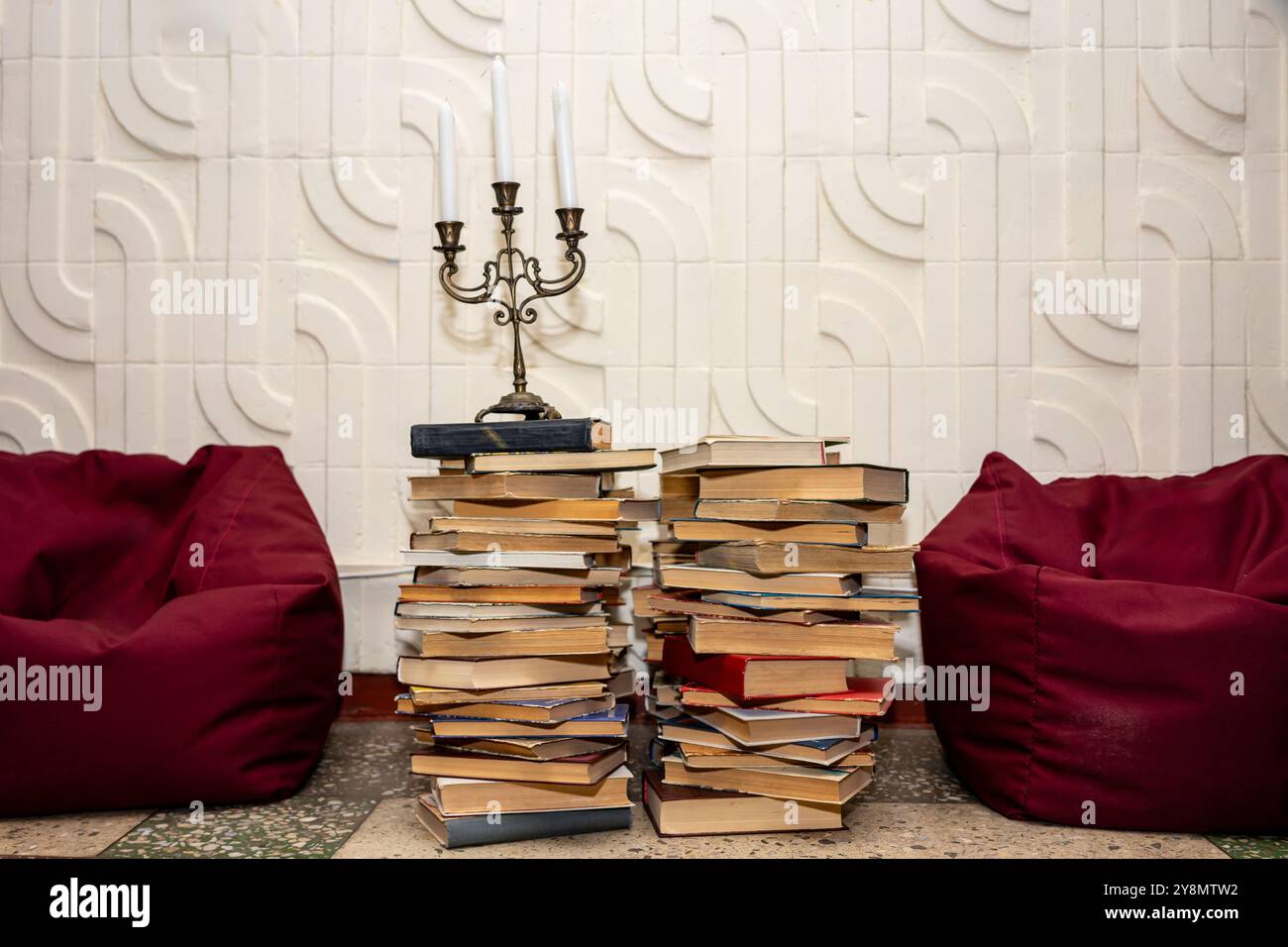 Ein alter Kerzenleuchter auf einem hohen Stapel Bücher zwischen roten Sitzsack-Stühlen. Stockfoto