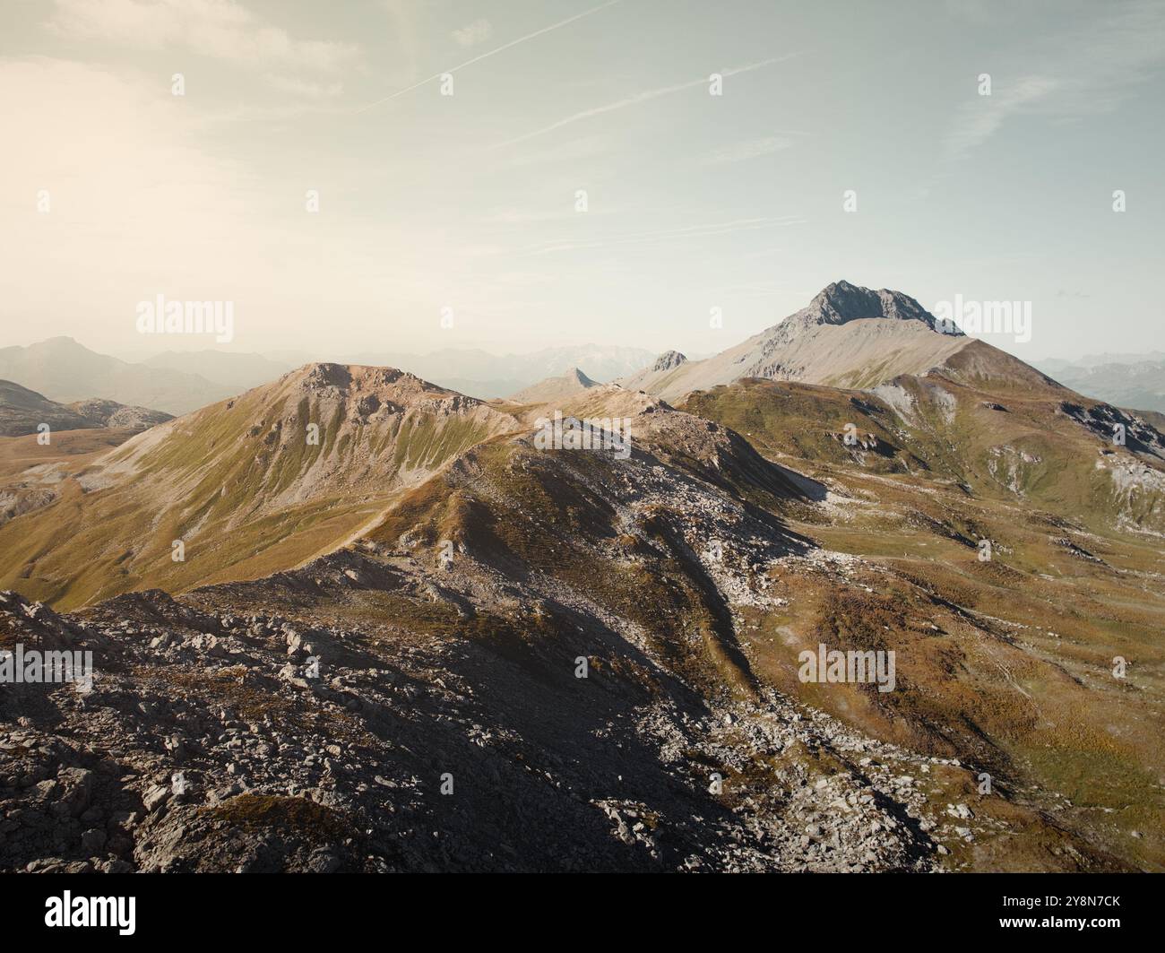 Drohnenblick auf die Savognin Berge in der Schweiz bei Sonnenuntergang mit Blick auf zerklüftete Gipfel und Täler, die in goldenes Licht getaucht sind Stockfoto