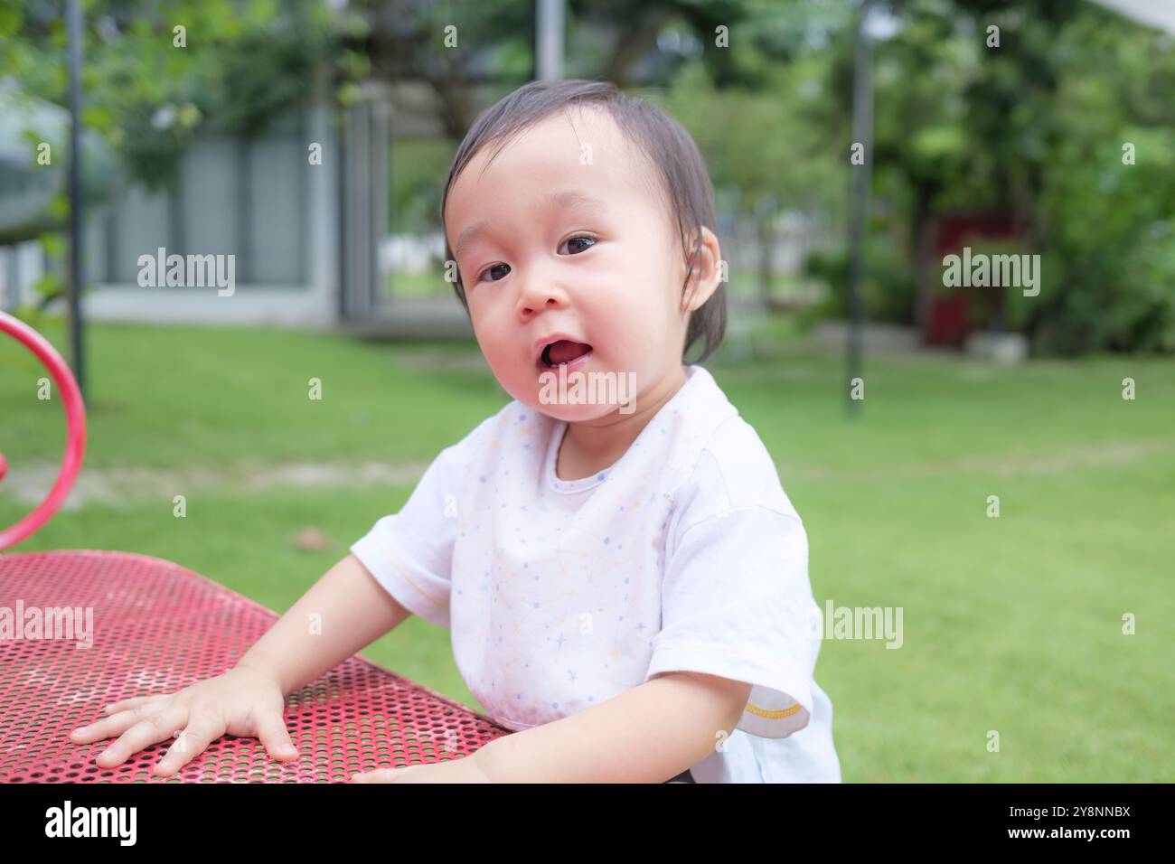 Fröhlicher asiatischer Kleinkinder, der Spaß auf dem Gras auf dem Spielplatz hat Stockfoto