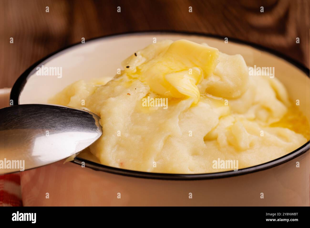 Frisch zubereitete Kartoffelpüree in einer Schüssel, mit einer schmelzenden Butterperle und einem Löffel, wunderschön auf einem dunklen Holztisch ausgestellt Stockfoto