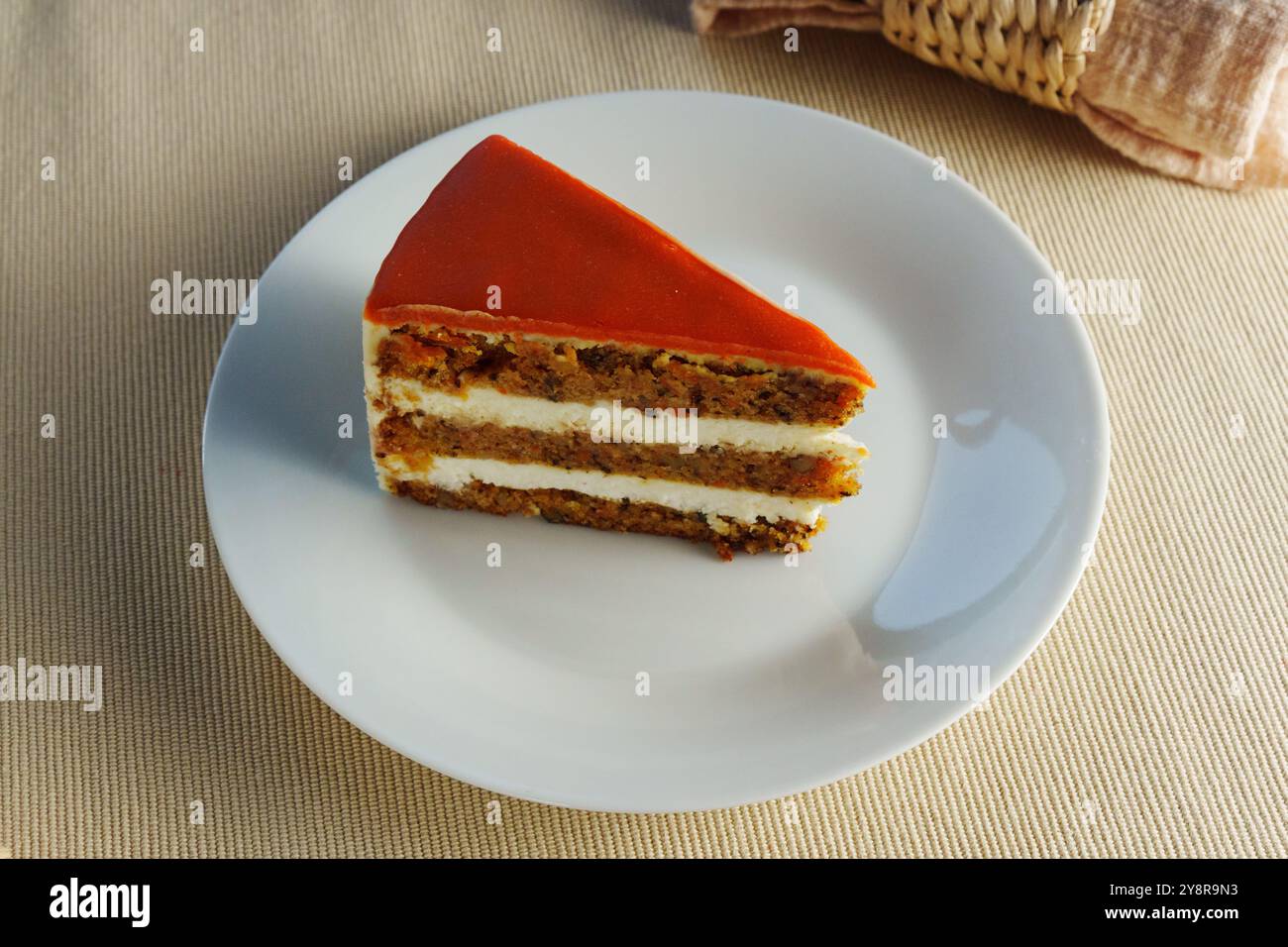 Köstliche Schichten Karottenkuchen mit cremigem Zuckerguss serviert auf einem weißen Teller in gemütlicher Atmosphäre Stockfoto