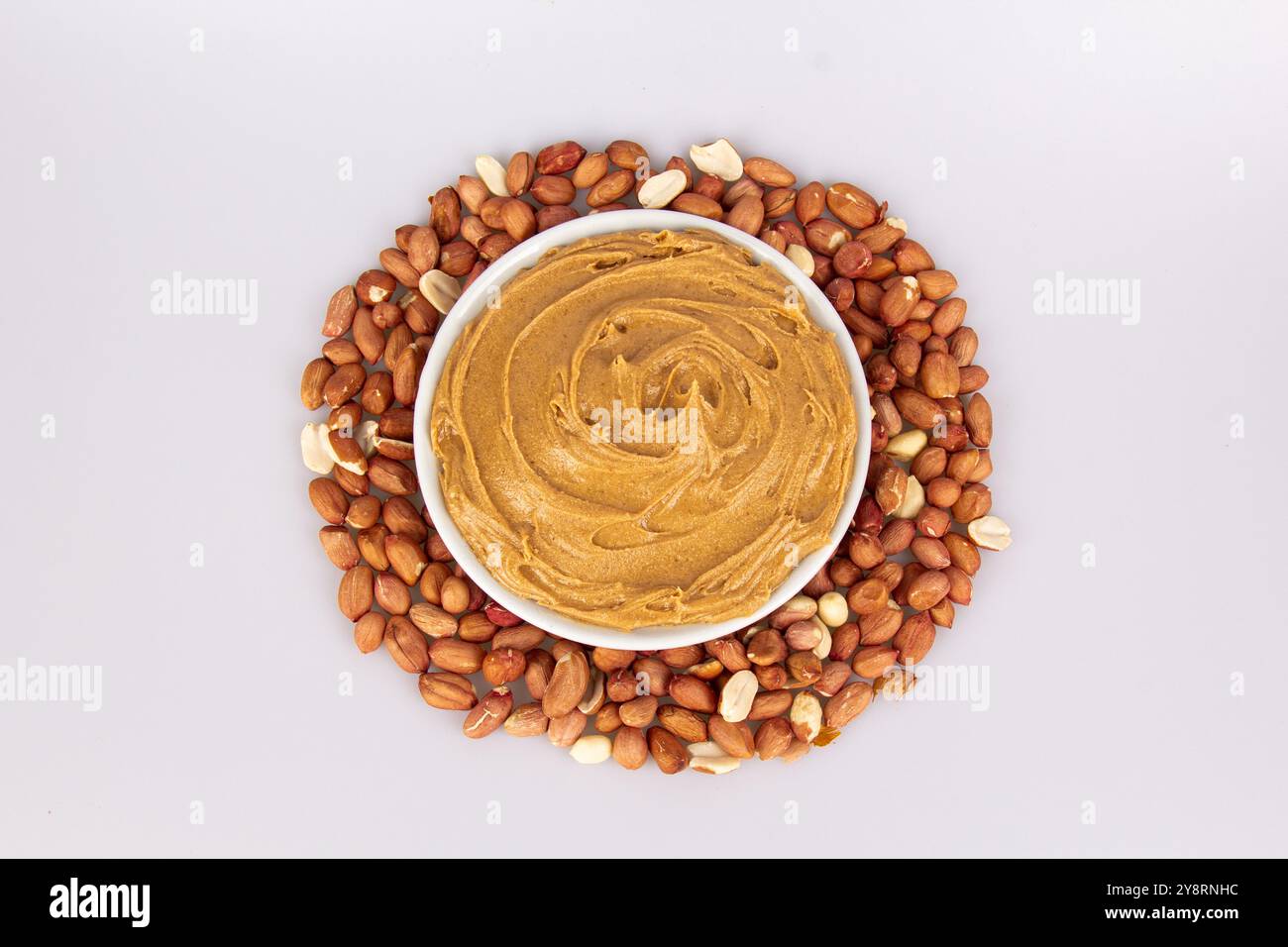 Cremige Erdnussbutter, Erdnussbutter in einem offenen Glasgefäß in der Mitte eines Erdnussfutterhintergrunds. Erdnüsse in der Schale, geschälte Erdnüsse auf einem weiß Stockfoto