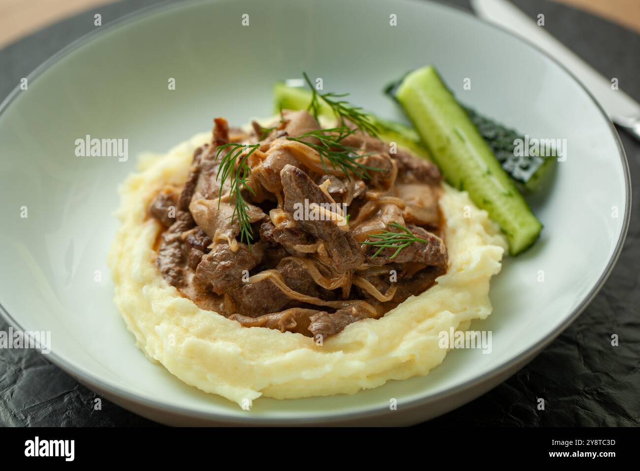 Köstliches Rindfleisch-Stroganoff mit Kartoffelpüree und Gurken, die auf einem Teller serviert werden Stockfoto