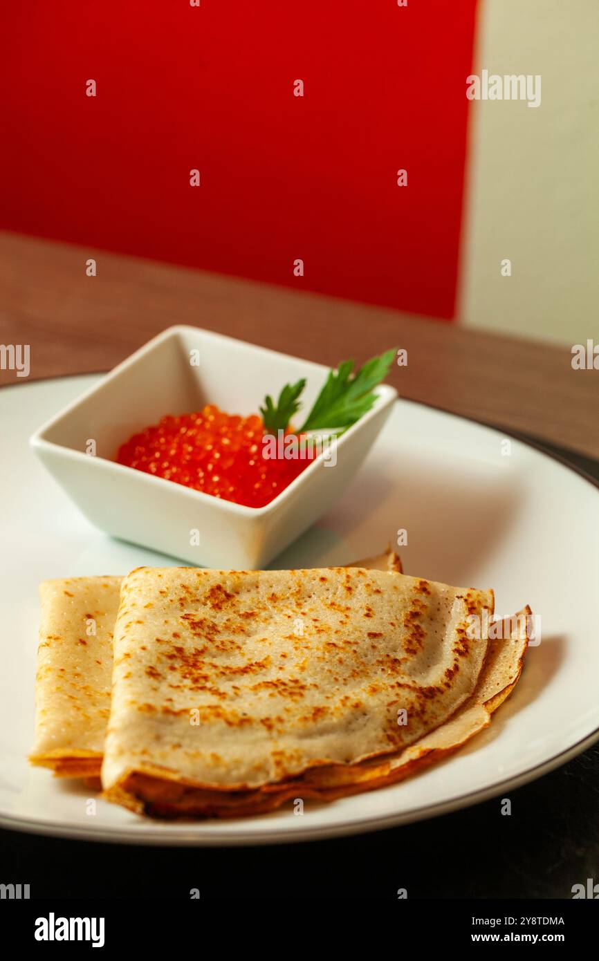 Traditionelle russische Pfannkuchen mit rotem Kaviar und Petersilie auf weißem Teller Stockfoto