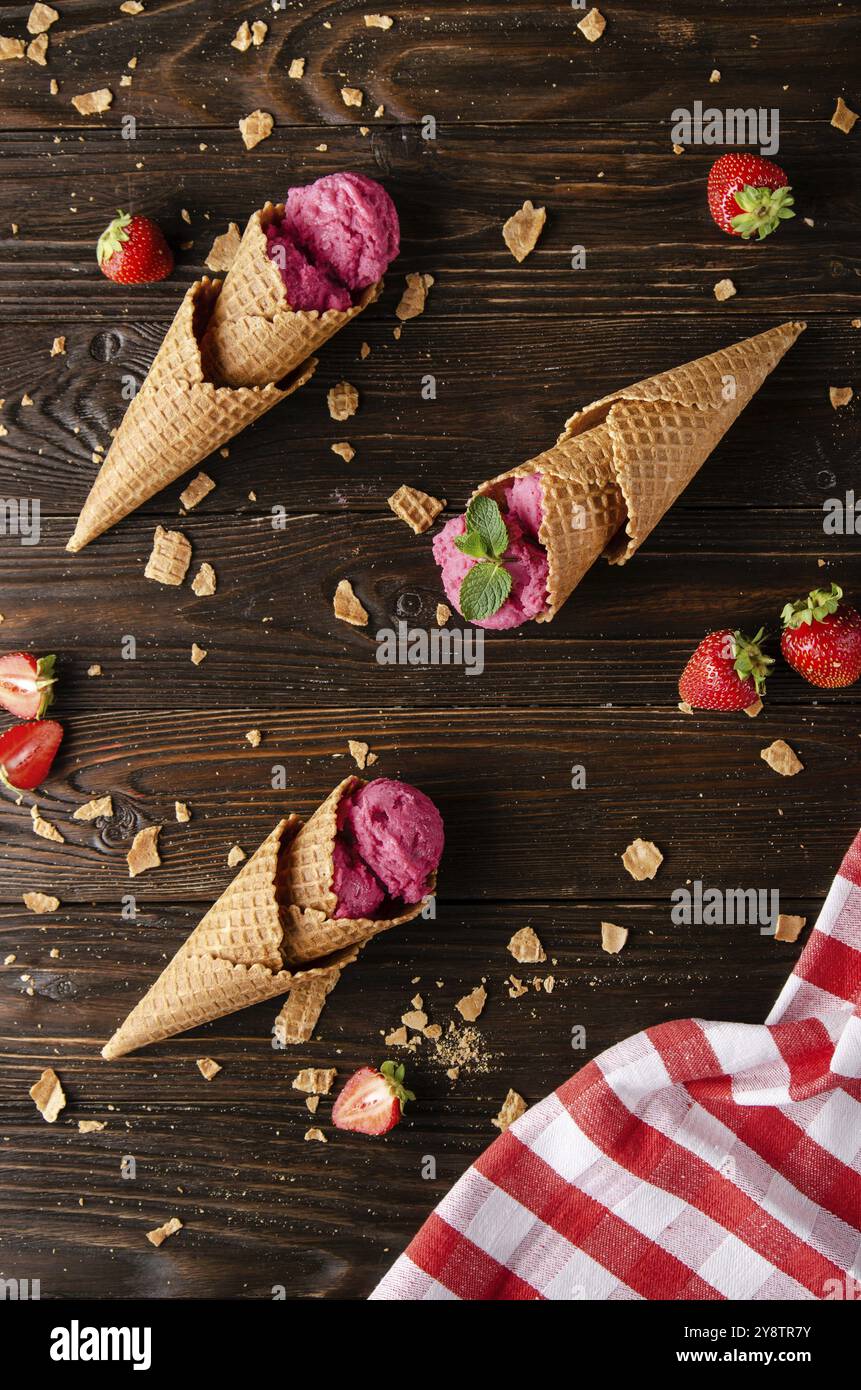 Waffelkegel mit Erdbeereis auf Holzküchentisch mit Krümel und Beeren zur Seite Stockfoto