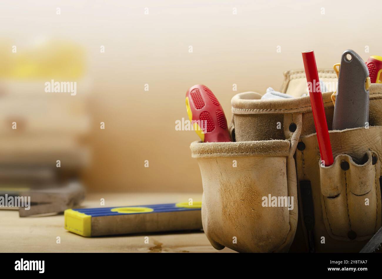 Gelber Werkzeuggürtel aus Leder mit Werkzeugen auf Sperrholz mit Ebenen- und Sicherheitsgläsern zur Seite Stockfoto