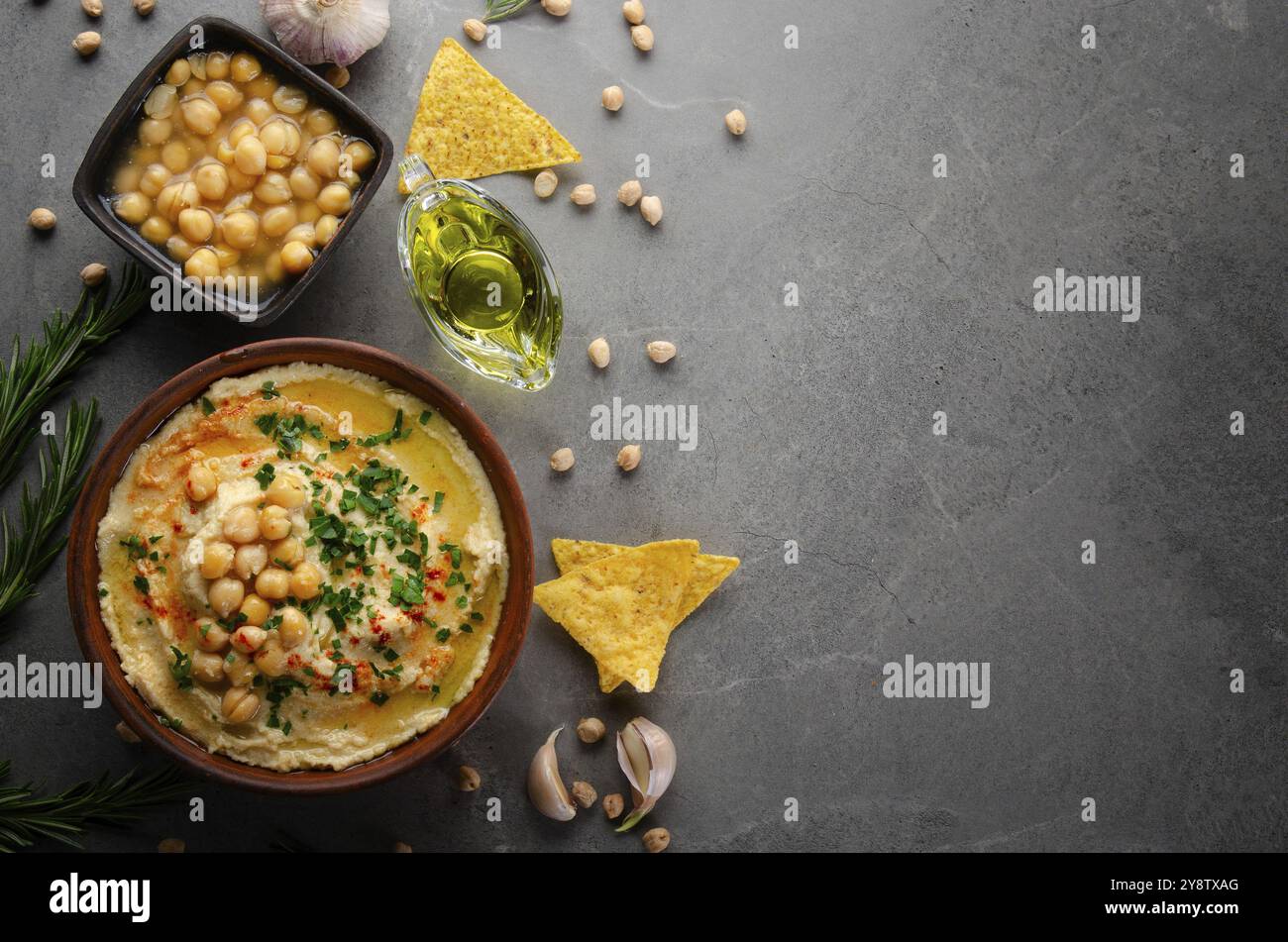 Flacher Laienblick auf Den Hummus in Tonschale mit Olivenöl, Kichererbsen und grünen Korianderblättern auf Steintisch serviert mit Ttortilla-Chips Stockfoto