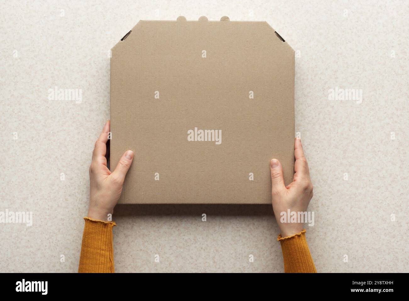 Pizza geschlossene Kartonbox in kaukasischen Händen auf Küchentisch flach Lay Mockup mit Kopierraum Stockfoto