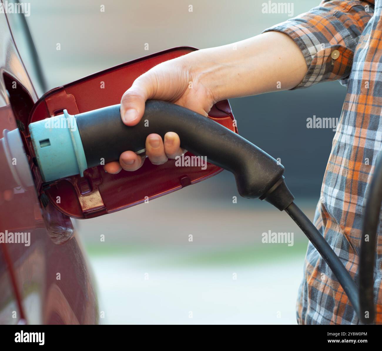 Das weibliche Modell steht neben einem Elektroauto und hält einen Ladestecker Stockfoto
