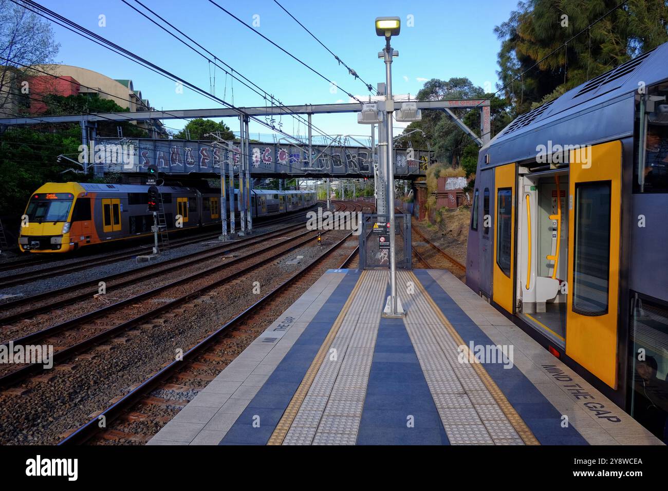 Ein Zug fährt auf dem Bahnsteig am Bahnhof Newtown, während ein anderer auf einem benachbarten Gleis im Vorort Newtown, Sydney, Australien, vorbeifährt Stockfoto