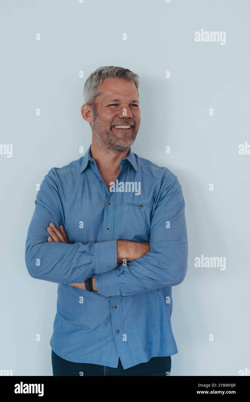 Junger Profi, der ein blaues Hemd trägt, steht vor weißem Hintergrund mit überkreuzten Armen. Hochwertige Fotos Stockfoto