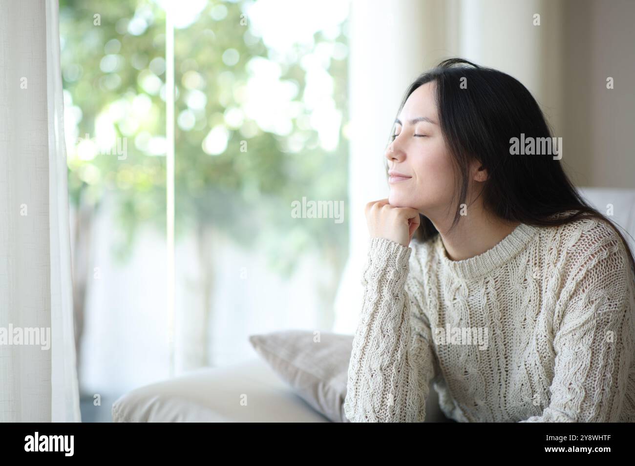 Asiatische Frau, die zu Hause auf einem Sofa sitzt und mit geschlossenen Augen entspannt Stockfoto